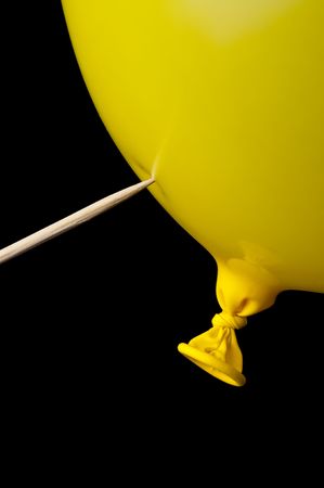 a pointed stick ready to pop a yellow balloon on blackの写真素材