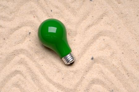 Green light bulb tossed on the sandの写真素材