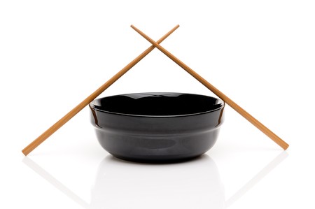 Crossed chopsticks on a black bowl on whiteの写真素材