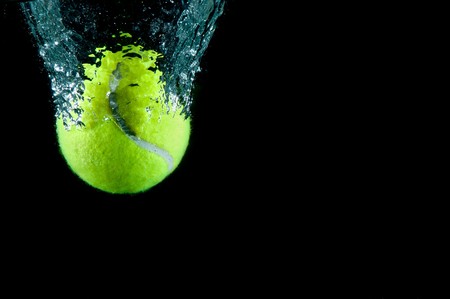 Tennis ball speeding through water on blackの写真素材