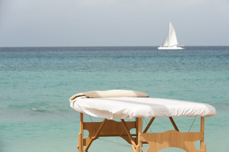 Massage table on a tropical beach with a sail boat on the horizonの写真素材