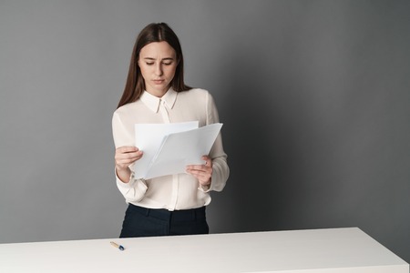 Businesswoman holds the papers in her hands and reads what is written there. Isolated on gray background.の写真素材