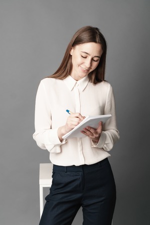 Portrait of businesswoman holding a notebook and pen in her hand. One is isolated on a gray background.の写真素材
