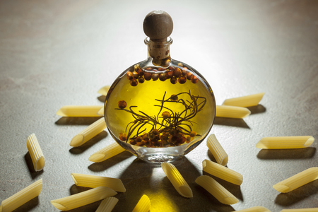 Bottle extra virgin olive oil with spices and some pieces of pasta on a ceramic backgroundの写真素材