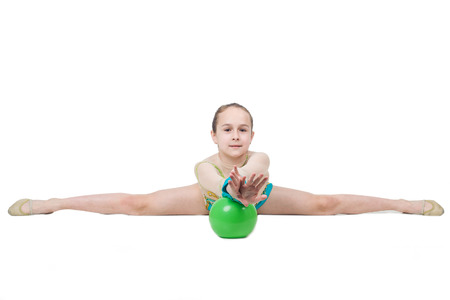 Little girl gymnast sits on split with green ball. Isolated on white background. Sporting exercise, stretch, flexibility, aerobicsの写真素材