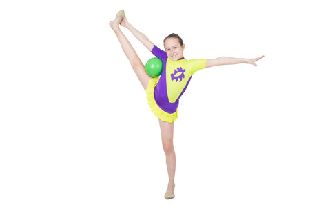 Cute young girl doing gymnastics with green ball isolated over whiteの写真素材