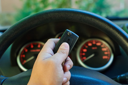 Man driver hand holding car key. Backlit gauges of an automobile. Orange glowing meters with a red needle. Fuel, tachometer, odometer and speedometer.の写真素材