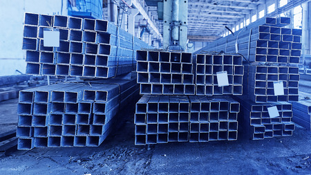 Metal pipes in a warehouse. Stacks of new square steel pipe in factory. Toned in cold toneの写真素材