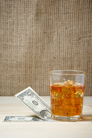 Dollars and glass of whiskey with ice on wooden table. Place for textの写真素材