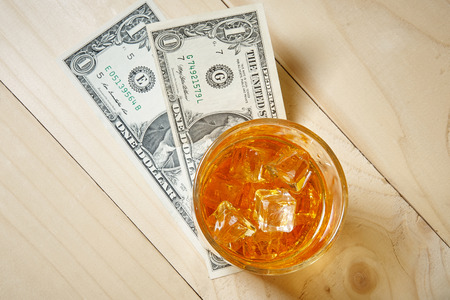 Dollars and glass of whiskey with ice on wooden table. Top view.の写真素材