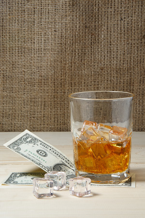 Dollars and glass of whiskey with ice on wooden tableの写真素材