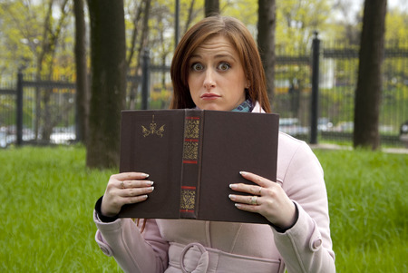 Beautiful redhead woman girl fooling around with a book in parkの写真素材