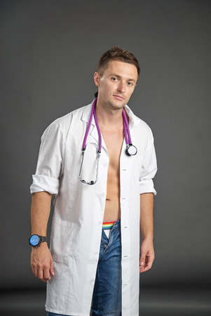 Portrait of a sexy young man in doctor costume with stethoscope around his neckの写真素材