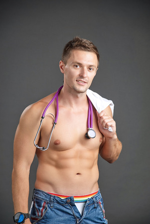 Portrait of a sexy young man with stethoscope around his neck and medical gown on shoulderの写真素材