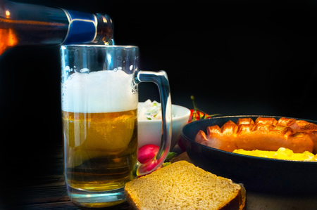 Bottle pours frothy beer into a glass amid a delicious dinnerの写真素材