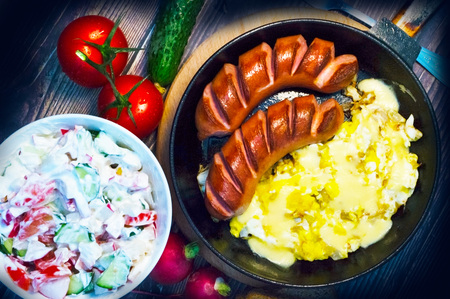 Frying pan with sausages, eggs, a plate with salad, on a wooden trayの写真素材