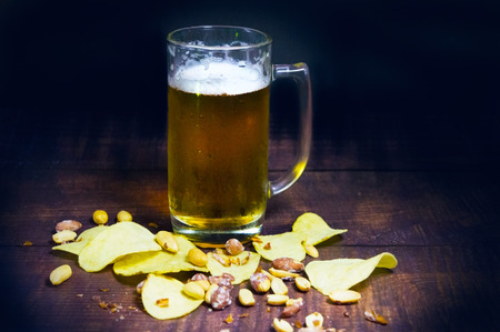 Glass of fresh beer, chips and nuts on a wooden tableの写真素材