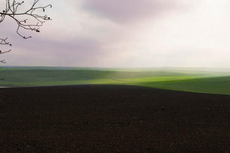 In the foreground is plowed land and green hills with a cloudy sky