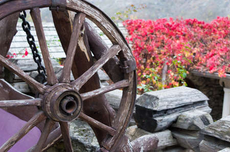 Old wheel from a cart on a background of red flowers.の写真素材
