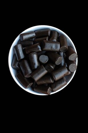 A white dish of black liquorice pieces isolated on a black backgroundの写真素材