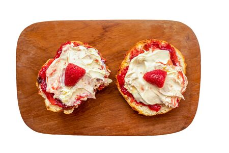 Two pieces of scone with strawberry jam and clotted-cream on a wooden board isolated on a white backgroundの写真素材