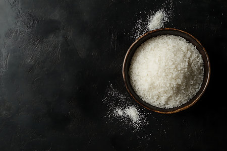 A top-down view of a bowl containing a generous amount of white flour. Some flour is scattered around the bowl, creating a rustic texture on the dark surface.の素材