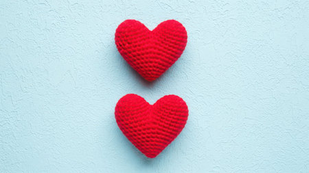 Two textured red knitted hearts are positioned vertically against a light blue background with a rough, uneven surface.の素材