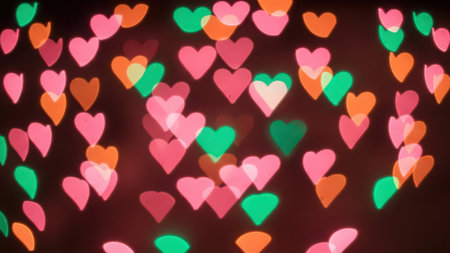 A dark background filled with out of focus heart shaped lights in pink, orange, and green. The lights are soft and glowing, creating a romantic and festive atmosphere.の素材