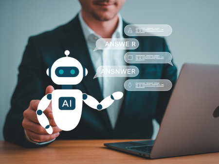 A man in a dark suit sits at a wooden desk with a laptop, interacting with a white AI robot with blue accents. The robot has a speech bubble with 'ANSWER' and other chat bubbles with......の素材