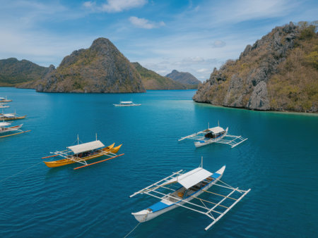 A serene scene of traditional Filipino outrigger boats floating on calm turquoise waters, surrounded by towering limestone cliffs and rocky mountains. The boats white or canvas-covered roofs......の素材