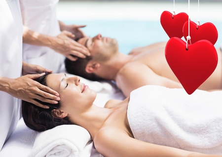 Composite image of couple getting spa treatment with heart shapes hanging in foregroundの写真素材