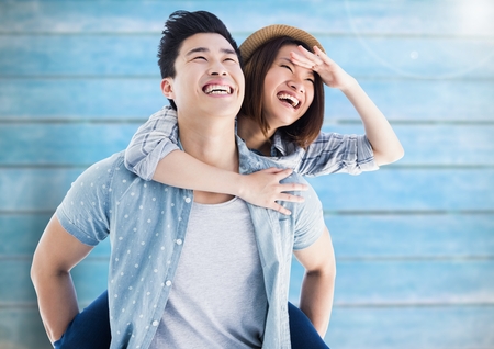 Composite images of happy man giving woman piggyback against wooden backgroundの写真素材