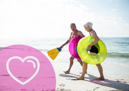 Composite image of senior couple on beach during vacation with heart shapeの写真素材