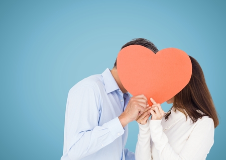 Romantic couple holding heart shape and kissing each other against blue backgroundの写真素材