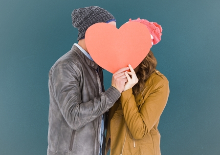 Romantic couple holding heart shape and kissing each other against blue backgroundの写真素材