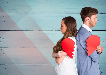 Sad couple holding broken heart against wooden backgroundの写真素材