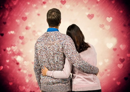 Rear view of couple standing with arm around against digitally generated heart backgroundの写真素材