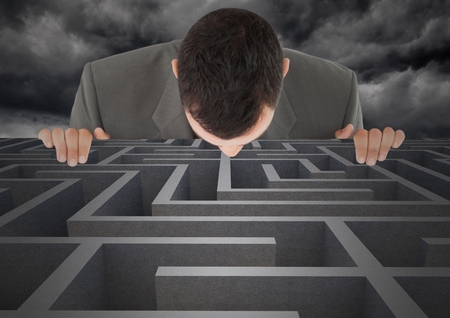 Businessman looking in maze against digitally composite cloudy backgroundの写真素材