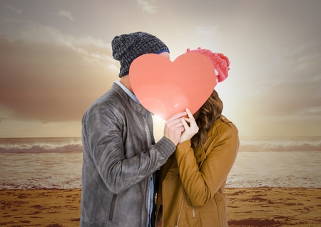 Couple kissing behind heart against digitally generated beach backgroundの写真素材
