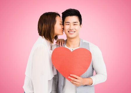 Woman kissing man while holding heart against pink backgroundの写真素材