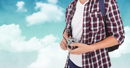 Mid section of man with backpack and digital camera against skyの写真素材