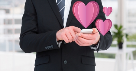 Mid section of businessman using mobile phone with digitally generated pink heartsの写真素材