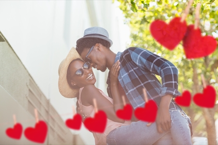 Composite image of red hanging hearts and affectionate couple embracing each other