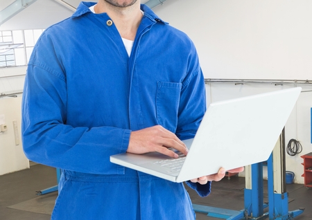 Mid section of mechanic using laptop in workshopの写真素材