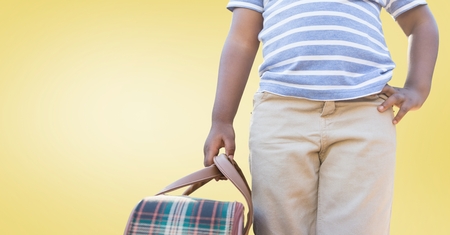 Mid section of boy standing with bag against yellow backgroundの写真素材