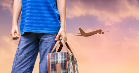 Composite image of man holding suitcase and plane flying in sunset skyの写真素材