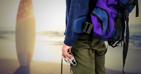 Mid section of tourist with camera, backpack and surfboard on beachの写真素材