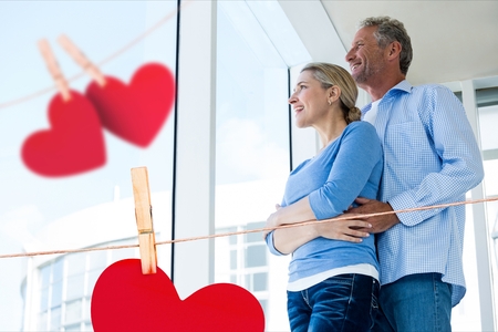 Composite image of couple embracing at home with hanging hearts aroundの写真素材