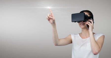 Smiling businesswoman talking on mobile phone while using virtual reality headset against grey backgroundの写真素材