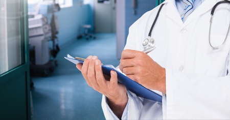 Mid section of doctor writing on clipboard in the hospital